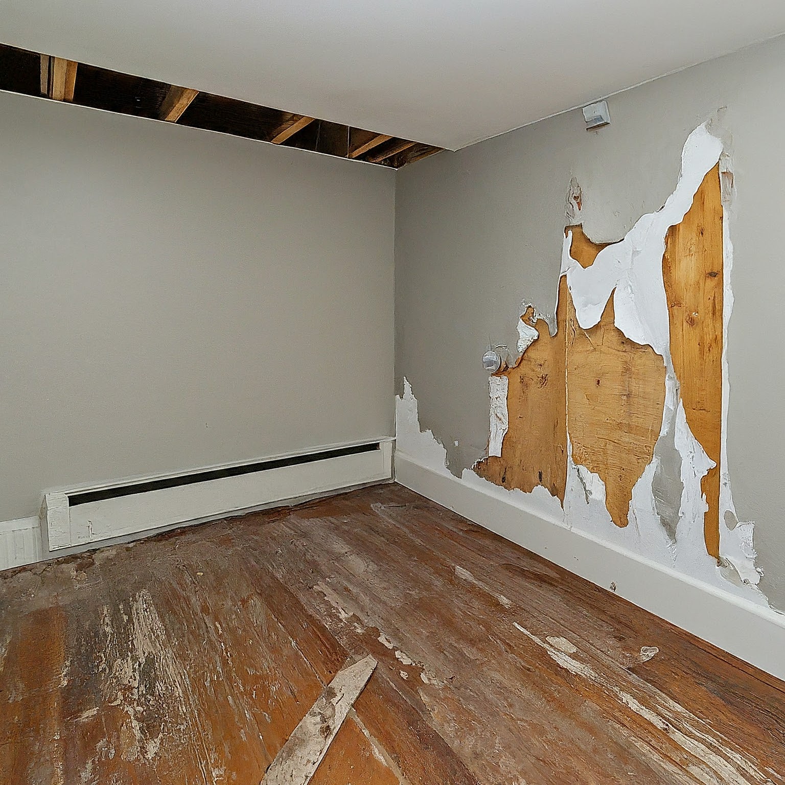A room with exposed ceiling beams, damaged walls with peeling paint and plaster, and a worn wooden floor reveals significant signs of disrepair, hinting at the need for mold restoration. -PureOneServices
