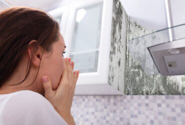 A woman covers her mouth in shock while looking at a mold-covered corner above a kitchen countertop, recognizing the urgent need for mold restoration. -PureOneServices