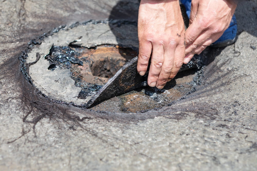 Worker lifts deteriorated roofing material during flat roof drainage system repair